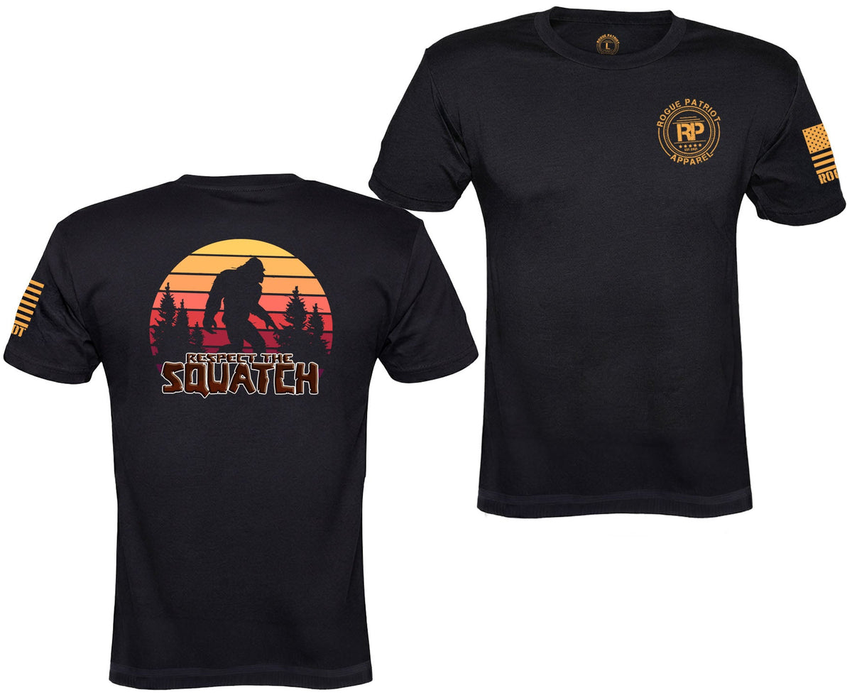 Two views of a black short-sleeve t-shirt on a white background. The left view shows a large back graphic with a silhouette of Bigfoot against a sunset gradient and the text 'IN THE LAND OF SQUATCHES'.