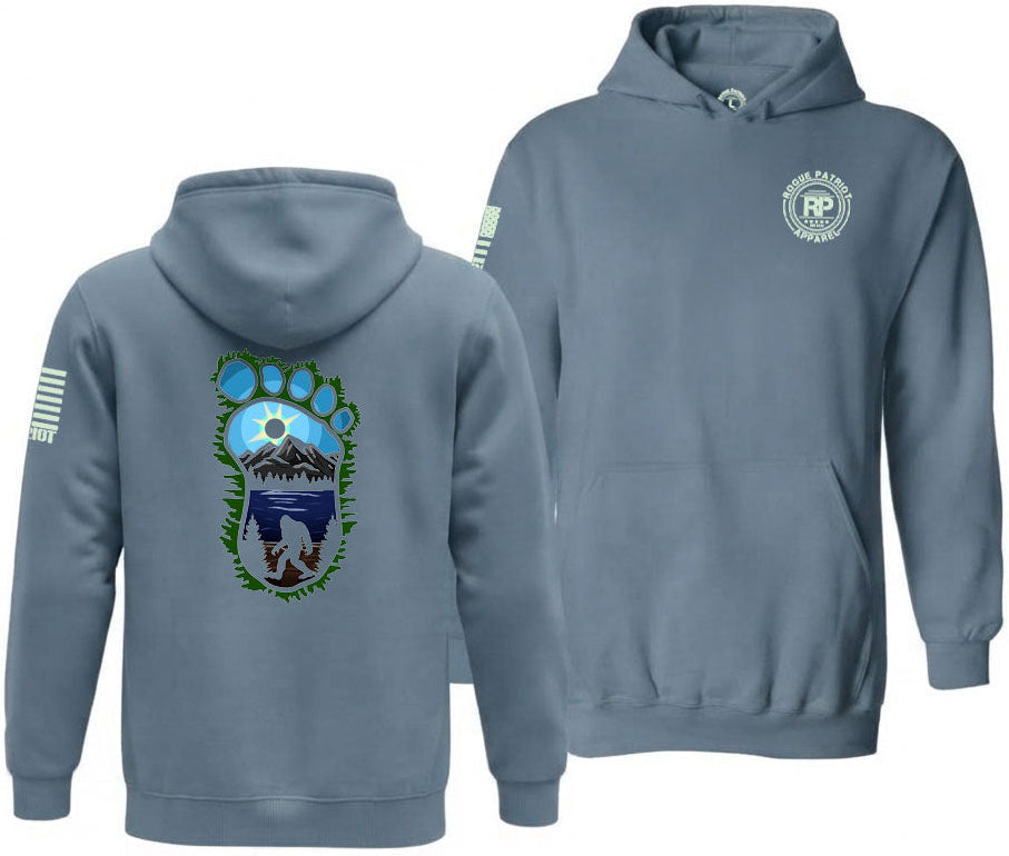 A slate blue hoodie shown from both the front and back views. The front features a circular 'RP' logo on the left chest, and the back displays a large graphic of a bigfoot print containing a mountain and lake design with green leaf accents.